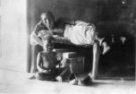 Žena ležící na lehátku v místnosti, na zemi sedí dítě, arabští kočovníci