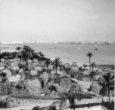 Bližší pohled na černošskou osadu na mořském břehu, s chýšemi a ohradami z rohoží