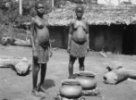 Dvě ženy stojí u velkých keramických nádob na podložkách na zemi, Bambuti