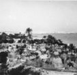 Černošská osada na mořském břehu na okraji města, s polokulovými chýšemi a ohradami z rohoží