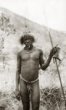 Muž kmene Tobur, na čepici má vysokou ozdobu z drátu, v ruce podhlavník a  oštěp
