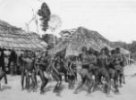 Tanečníci mezi chýšemi – lovecký mužský tanec „goma“, Bambuti