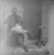 Městsky oblečený muž sedí na židli thonetce u malého kulatého stolku