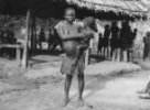 Žena s dítětem u boku stojící před přístřeškem, Bambuti