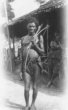 Stojící muž s lukem a šípy, sukénku přidržuje evropský opasek s přezkou, Babira nebo Balese
