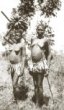 Dvě vdané ženy v sukénkách, jedna nese na hlavě trs banánů, druhá má přes  rameno nádobu z tykve, Gišu (Mugišu, Bagišu)